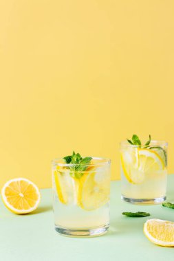 Sarı ve yeşil zemin üzerinde nane yaprakları olan iki bardak buzlu limon suyu. Sodayla taze yaz içeceği..