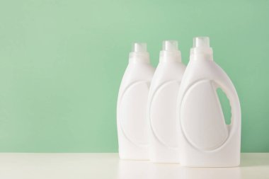 Beyaz plastik şişeler, sıvı çamaşır deterjanı, temizlik maddesi, çamaşır suyu ya da yumuşatıcı. Yeşil arka planda biyolojik yıkama ürünü için boş model paketleme. Çamaşır günü