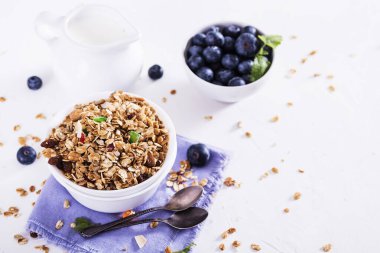 Beyaz ahşap arka planda bir kasede mavi böğürtlenli müsli. Lezzetli ve sağlıklı kahvaltı..