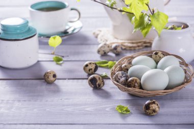Mavi yumurtalı Paskalya kompozisyonu, bir fincan çay ve beyaz arka planda yeşil yapraklı bahar ağacı dalları. Seçici odak.