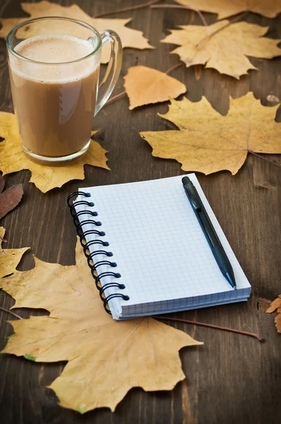 笔记本和杯咖啡与秋天叶子上木制辩识产生的背景 免版税图库图片