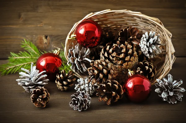 Christmas concept (decoration). Basket with red ball and cone  on rustic wooden background — Stock Photo, Image