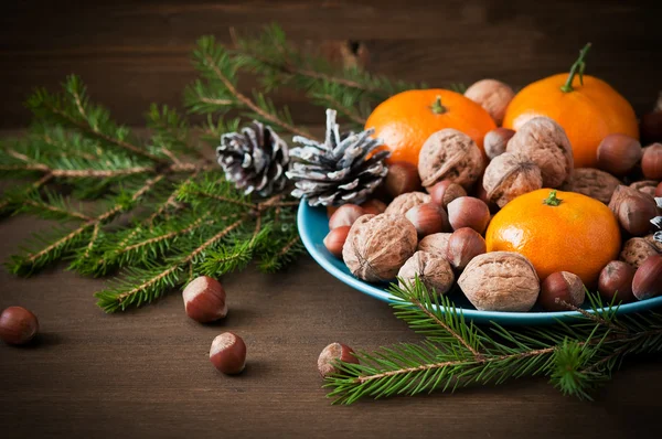 Concept de Noël (décoration). Assiette avec mandarine, cône et noix sur fond bois rustique — Photo