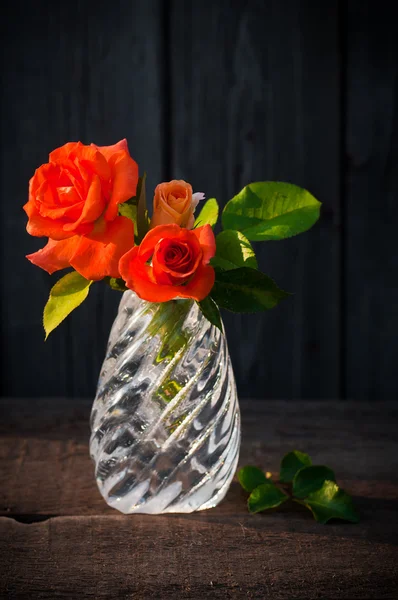 Jarrón de cristal con rosas naranjas en la vieja mesa de madera — Foto de Stock