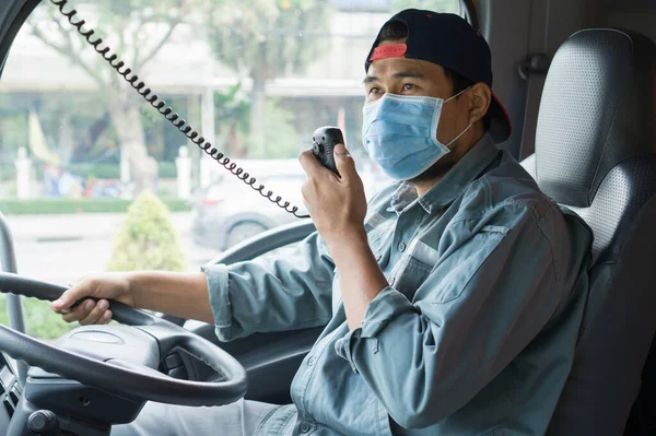 Young Asian man wearing protective mask During driving. professional truck driver using radio communicate and talk. Smile and service with friendship of Truck driver, transportation and delivery