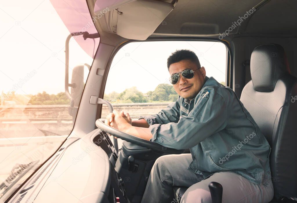 semi-truck driver wearing sunglasses happy smiling in cockpit.