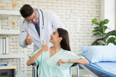 Beyaz erkek doktor, Asyalı hasta ile görüşüyor ve klinikte samimi bir şekilde gülümsüyor. Hastalık teşhisi, sağlık kontrolü, hastanede tıbbi konsültasyon -.