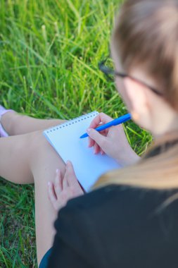 çimenlerin üzerinde oturan ve bir defterde yazılı kadın
