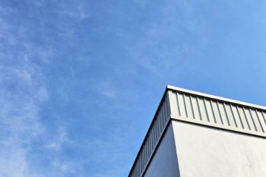 Açık mavi gökyüzünün altında ayakta duran dikişli metal kaplamalı modern bina.