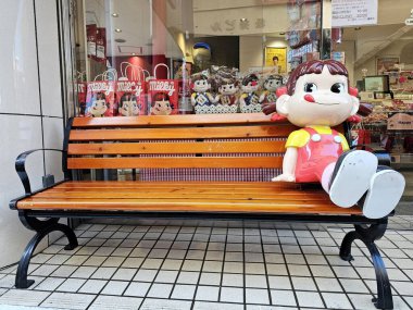 Kamakura, Japonya - 16 Ocak 2026: Fujiya markasının ikonik maskotu Peko chan, bir dükkanın önündeki ahşap bankta oturuyordu..