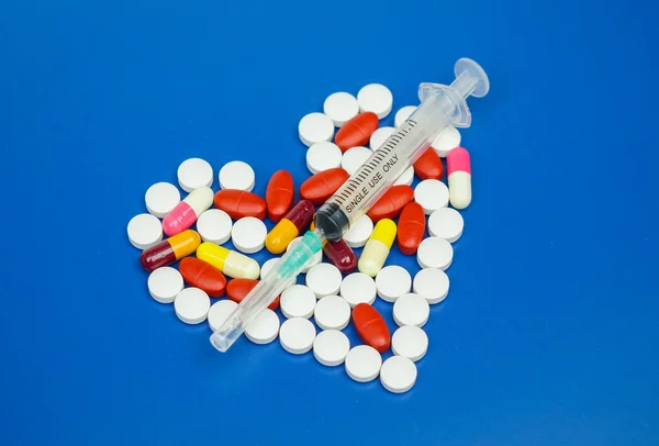 Jeringa sobre medicamentos dispuestos como una forma de corazón — Foto de Stock