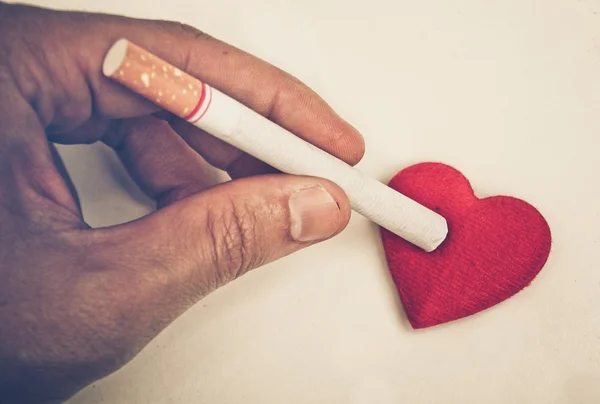 Hand with cigarette burnt a red heart — Stock Photo, Image