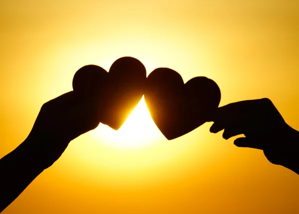 Mãos segurando corações contra o pôr do sol — Fotografia de Stock