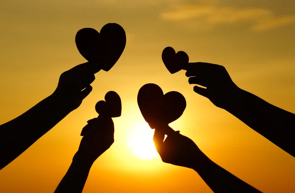 Hands holding hearts against sunset — Stock Photo, Image