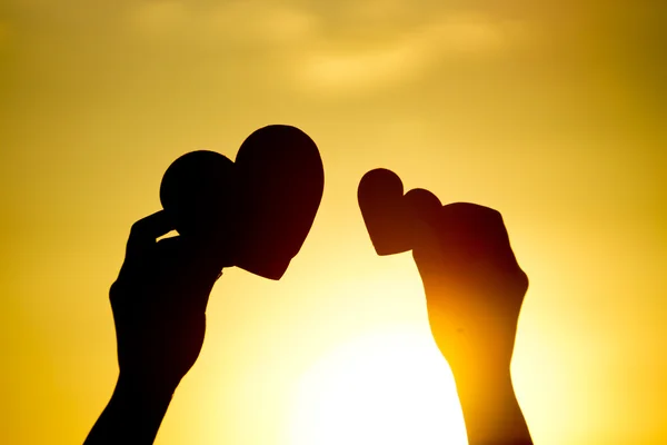 Manos sosteniendo corazones contra el atardecer — Foto de Stock