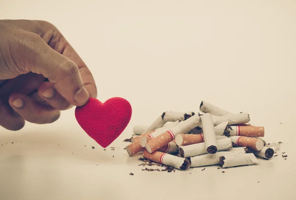 Hand picks up heart next to cigarettes — Stock Photo, Image