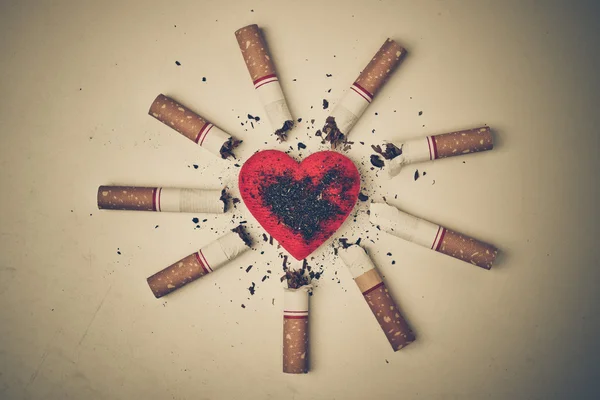 Cigarrillos quemados alrededor de un corazón rojo — Foto de Stock