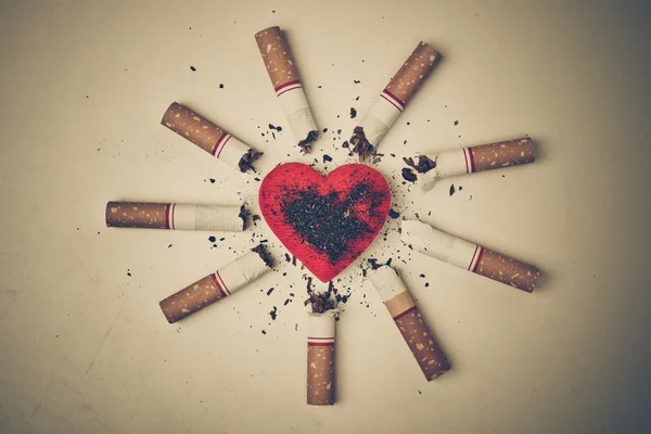 Burnt cigarettes around a red heart — Stock Photo, Image