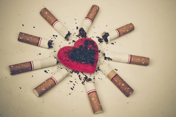 Cigarrillos quemados alrededor de un corazón rojo — Foto de Stock