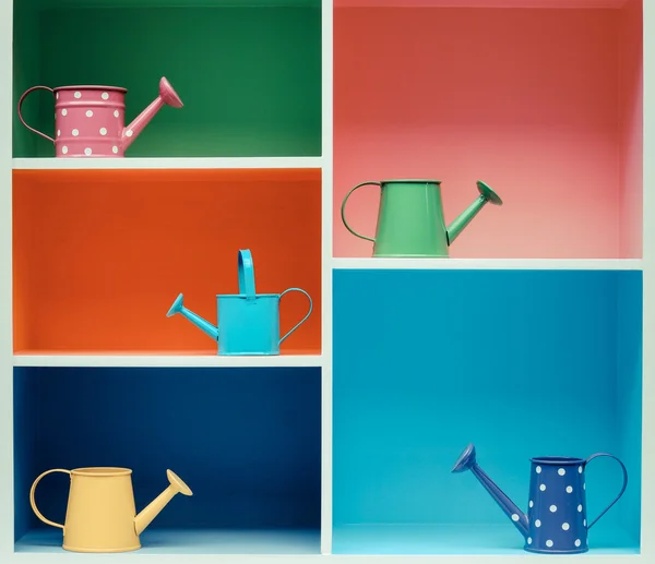 Watering cans on colorful shelf — Stock Photo, Image