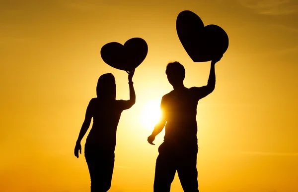 Ένας άνδρας και μια γυναίκα που κρατά μεγάλο κόκκινες καρδιές με φόντο ηλιοβασίλεμα σιλουέτα — Φωτογραφία Αρχείου