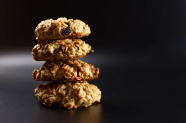 Siyah arka planda kuru üzümlü ev yapımı yulaflı kurabiye yığını.