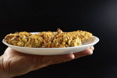 El, siyah arka planda kuru üzümlü ev yapımı yulaf ezmeli kurabiye tabağı tutuyor.