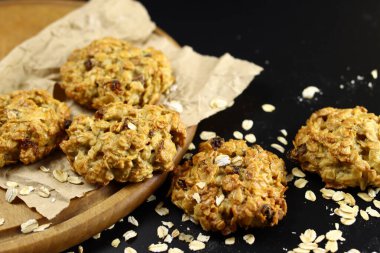 El yapımı yulaf ezmeli kurabiyeler, kara arka planda el işi kağıt üzerinde kuru üzümler.