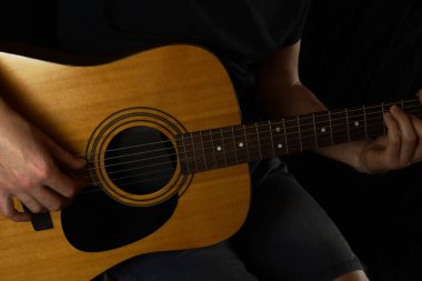 Adam siyah arka planda akustik gitar çalıyor.
