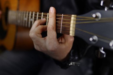 Deri ceketli siyah arka planda gitar çalan bir müzisyen.