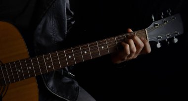 Deri ceketli siyah arka planda gitar çalan bir müzisyen.