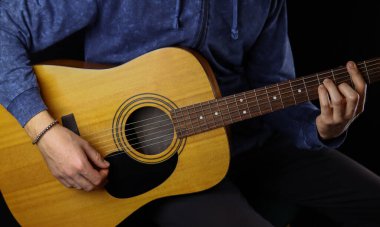 Adam siyah arka planda akustik gitar çalıyor.