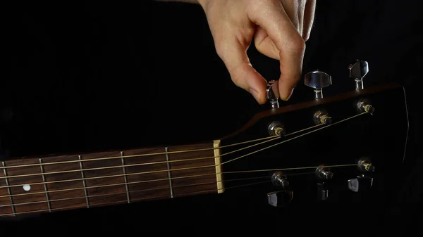 musician guitar player tunes guitar, hand close-up on black background