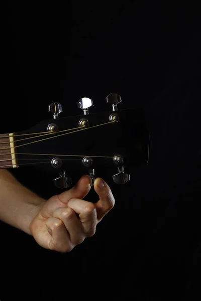 musician guitar player tunes guitar, hand close-up on black background. vertical orientation