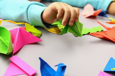 Çocuk renkli kağıtlardan origami el sanatları yapıyor, elleri yakın plan.