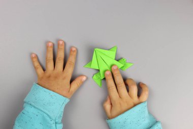 Çocuk renkli kağıtlardan origami el sanatları yapıyor, elleri yakın plan.