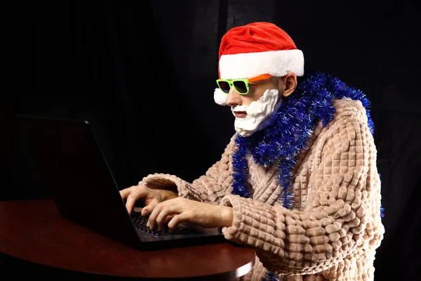 Slechte Gekke Kerstman Zonnebril Schuimbaard Huiskleding Zittend Aan Een Laptop — Stockfoto
