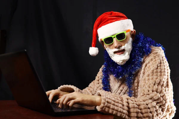 Slechte Gekke Kerstman Zonnebril Schuimbaard Huiskleding Zittend Aan Een Laptop — Stockfoto