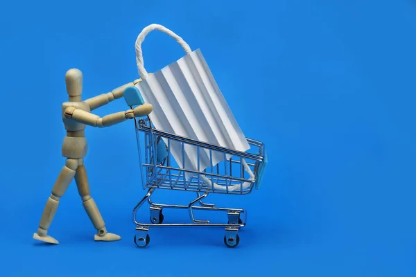 Wooden man carrying Shopping cart with medical protective bandage on a blue background.