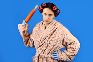 Bukleli kızgın genç ev hanımı elinde oklavayla