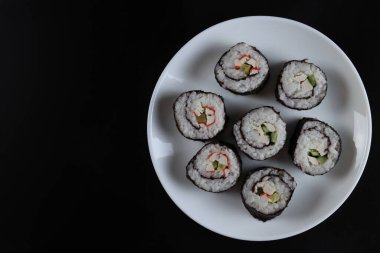 Salatalıklı taze suşi ruloları, siyah arka planda yengeç çubukları.