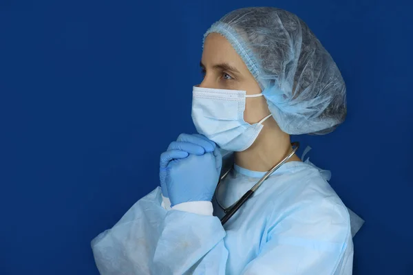 praying doctor in medical mask and cap on blue background