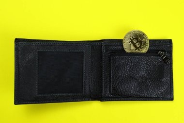 Sarı arka planda siyah deri bir cüzdanda altın bitcoin.
