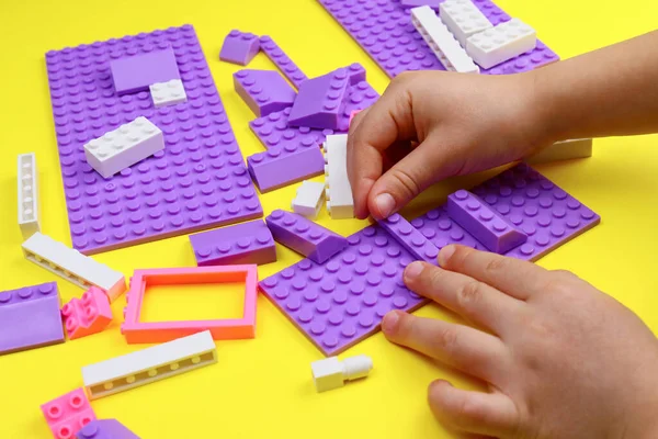 child plays with colored toy blocks on a yellow table