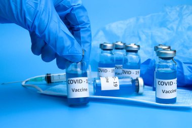 Doktor elinde mavi arka planda bir koronavirüs aşısı tutuyor. Ncov COVID-19 salgınıyla mücadele kavramı