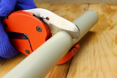 Eldivenli el, ahşap zeminde makasla pvc su borusunu keser.
