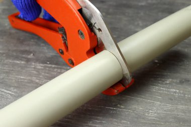 Eldivenli el, gri arka planda pvc su borusunu makasla keser