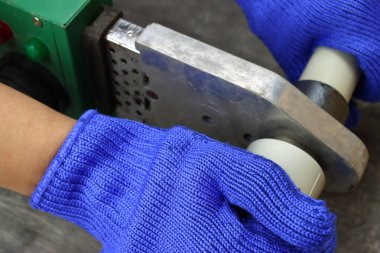 Eldivenli tesisatçı plastik pvc borular lehimliyor.