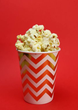 caramel popcorn in a paper cup on a red background. Vertical orientation