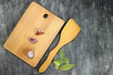 Wooden cutting board with garlic and bay leaves on a gray table